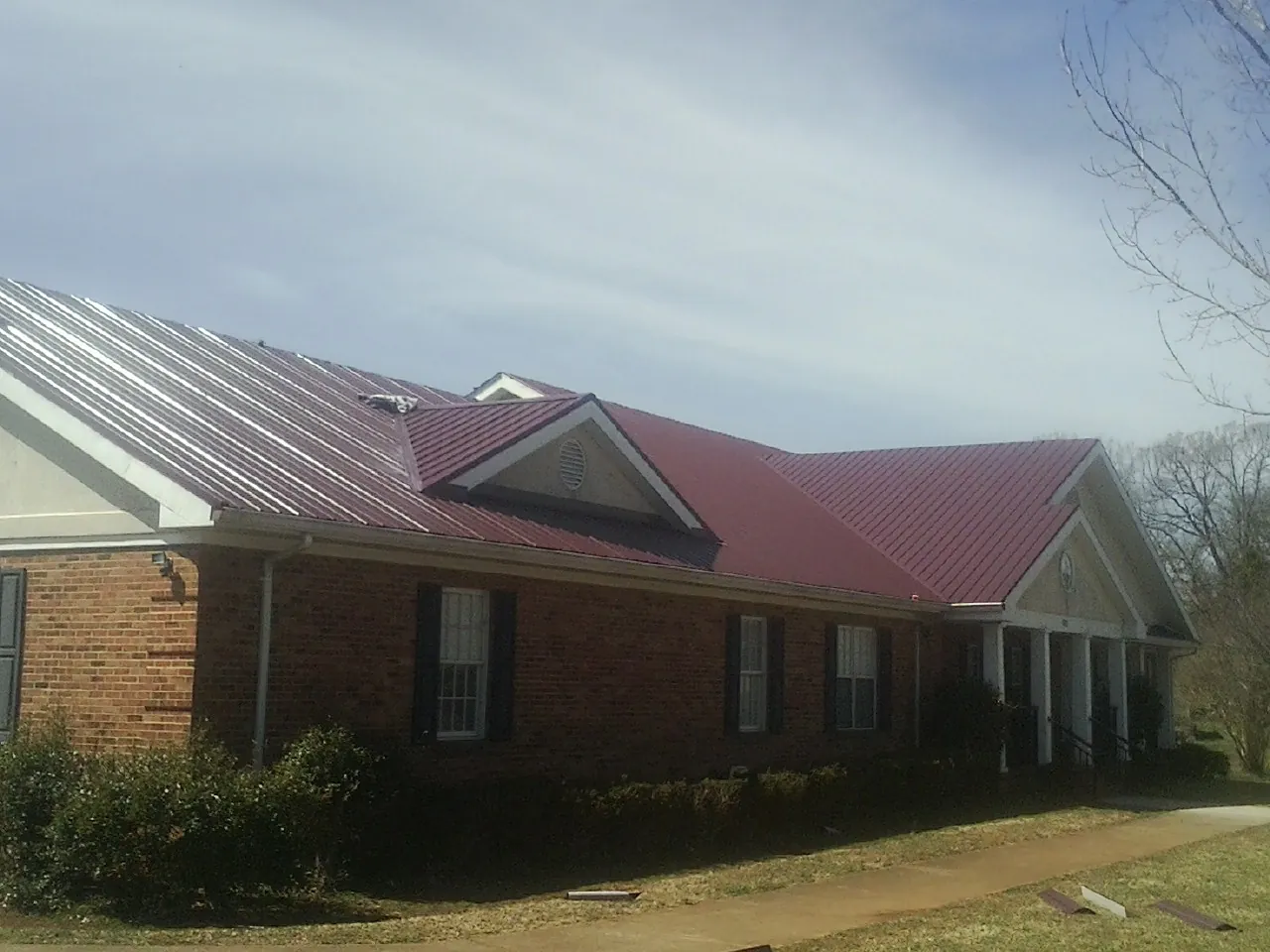 Red metal roof with gabled entries on a long brick building, from a Hail Damage Roof Repair job in Warrenton